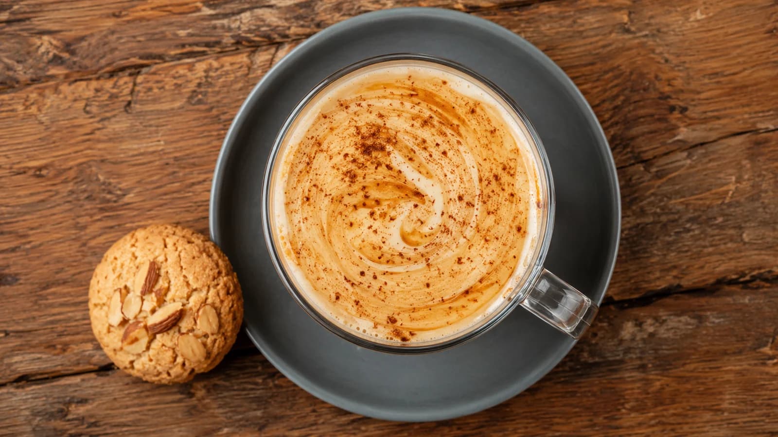 Cafe bombon stirred with cinnamon beside an almond cookie on a wooden table