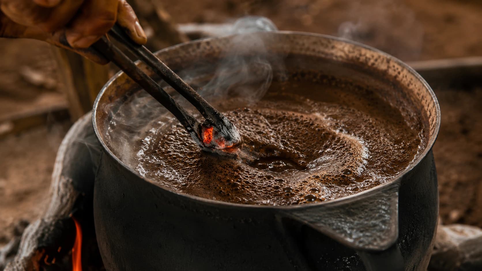 Glowing ember being added to boiling unfiltered cafe tropeiro coffee with metal tongs
