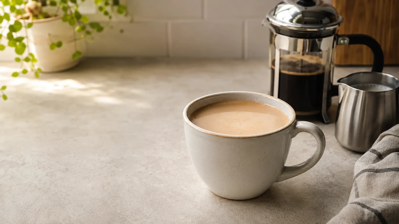 Caffe misto in a ceramic mug with brewed coffee, steamed milk, and a French press nearby
