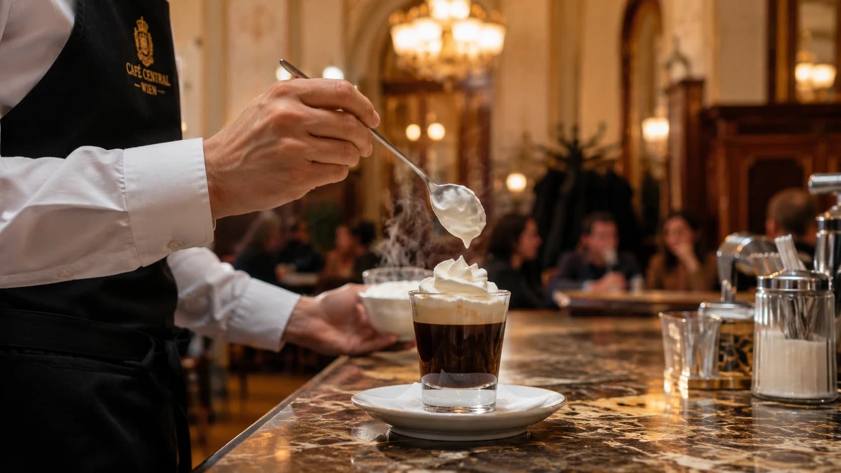 Whipped cream being spooned onto strong black coffee to prepare an Einspanner