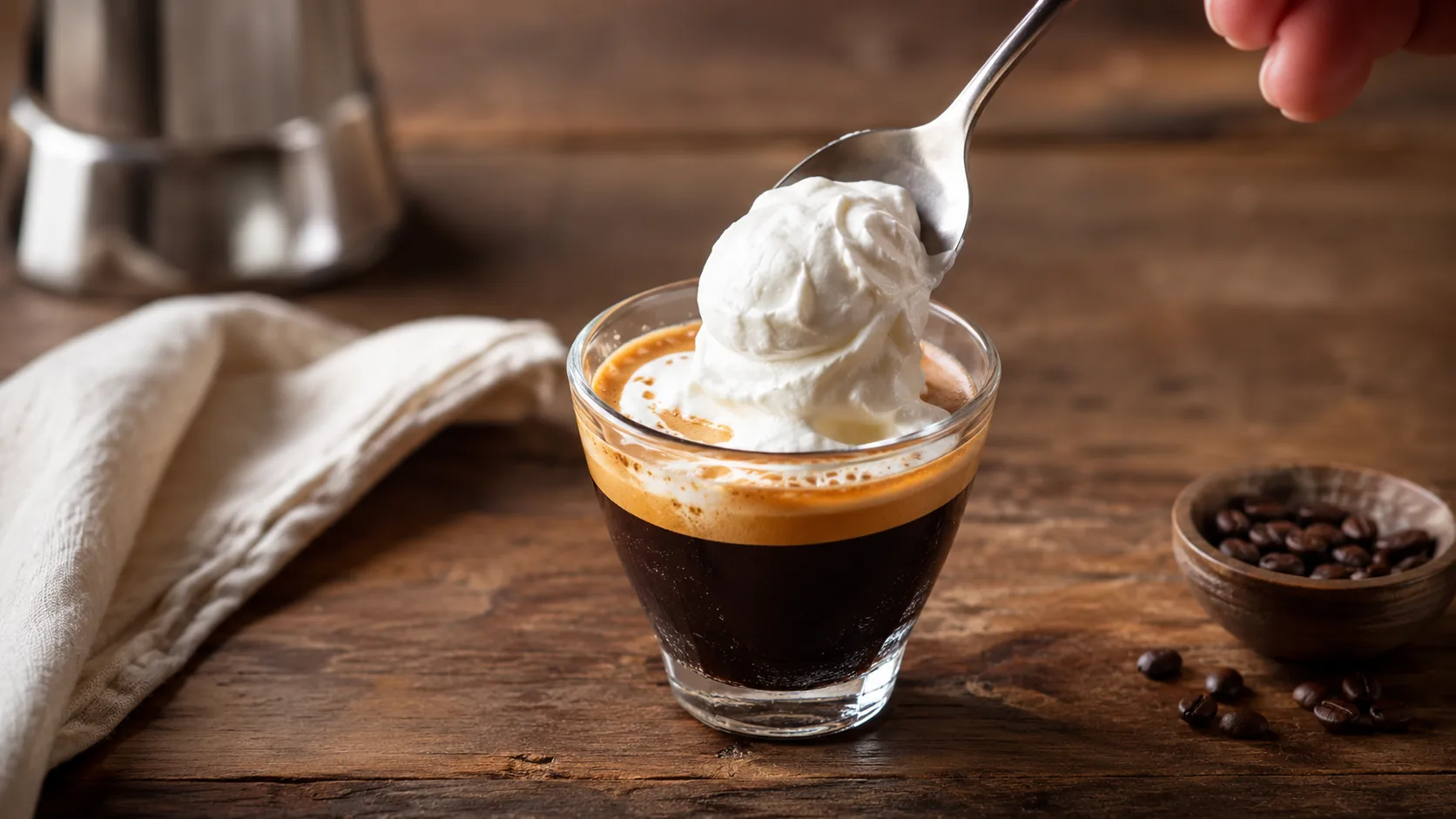Whipped cream being spooned onto espresso for espresso con panna