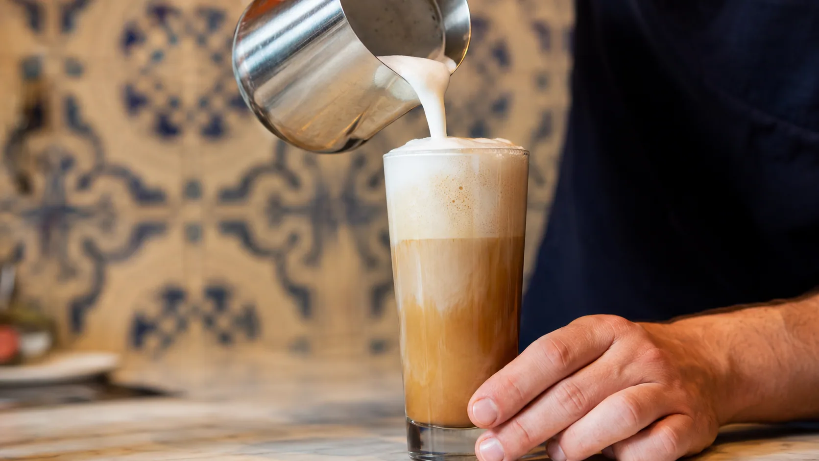 Lightly foamed milk being poured into a tall glass of Portuguese Galão coffee