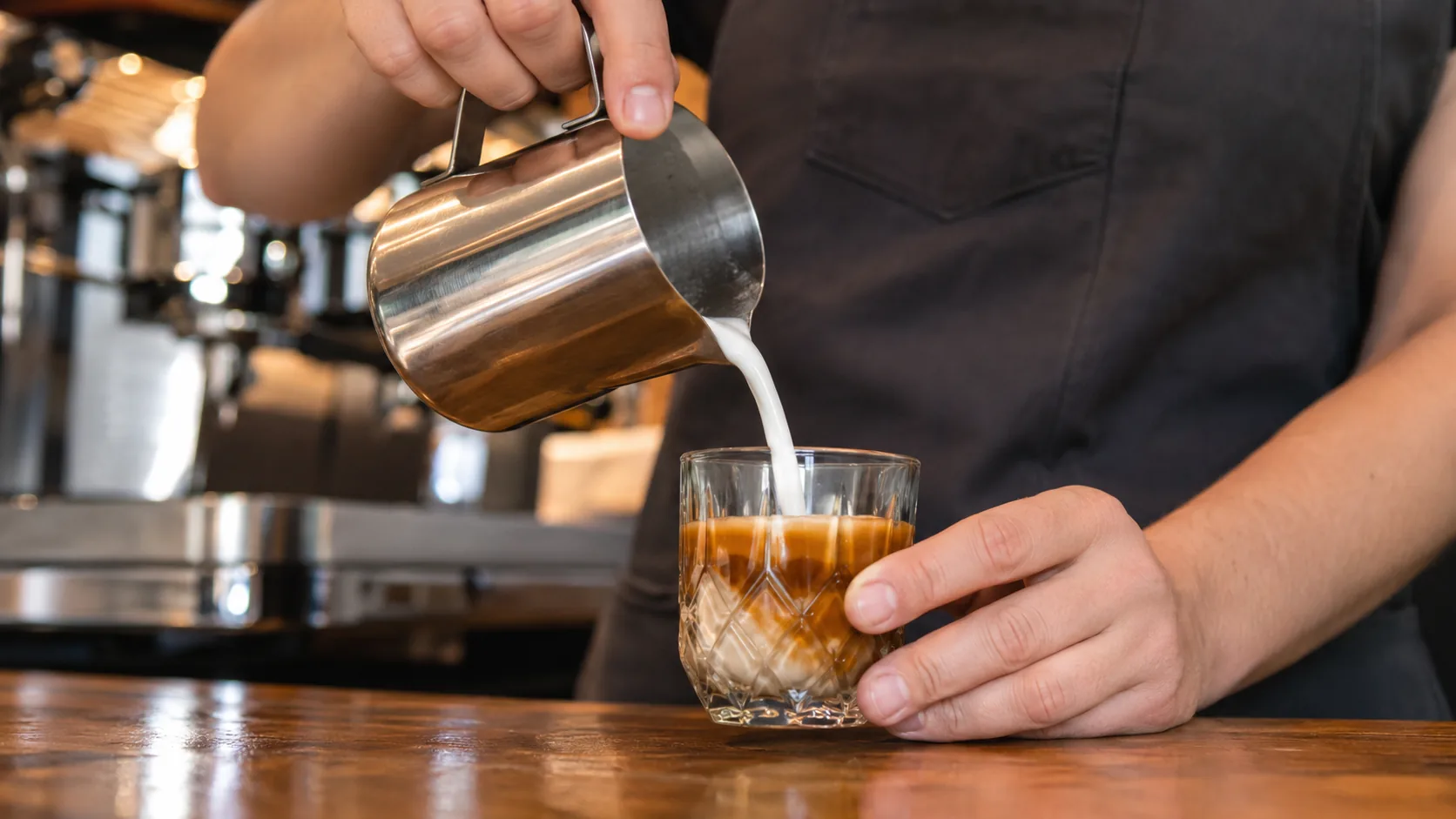 Steamed milk being poured into espresso in a faceted glass for Gibraltar coffee