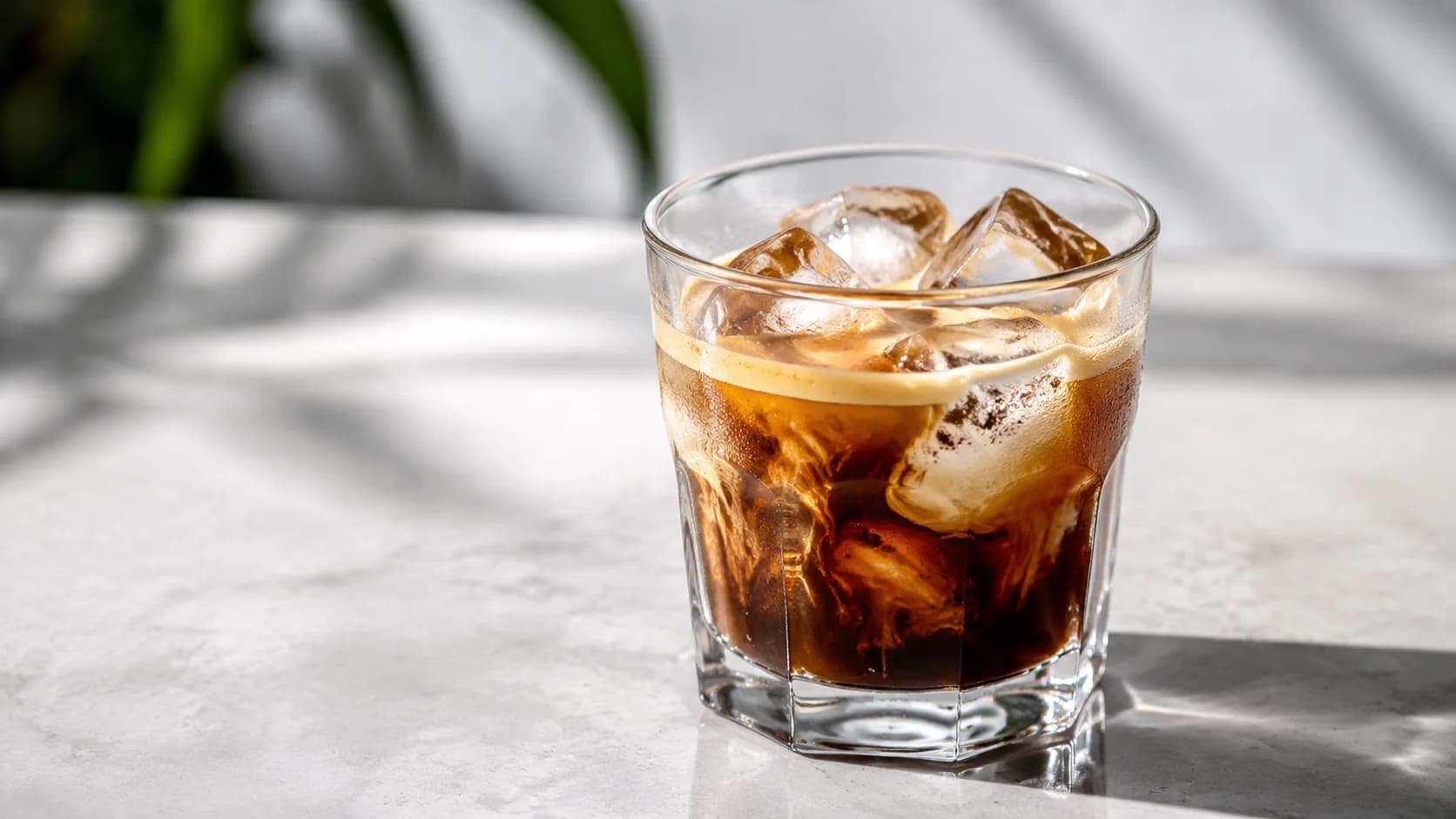 Double iced espresso with crema swirling around large ice cubes in a small glass