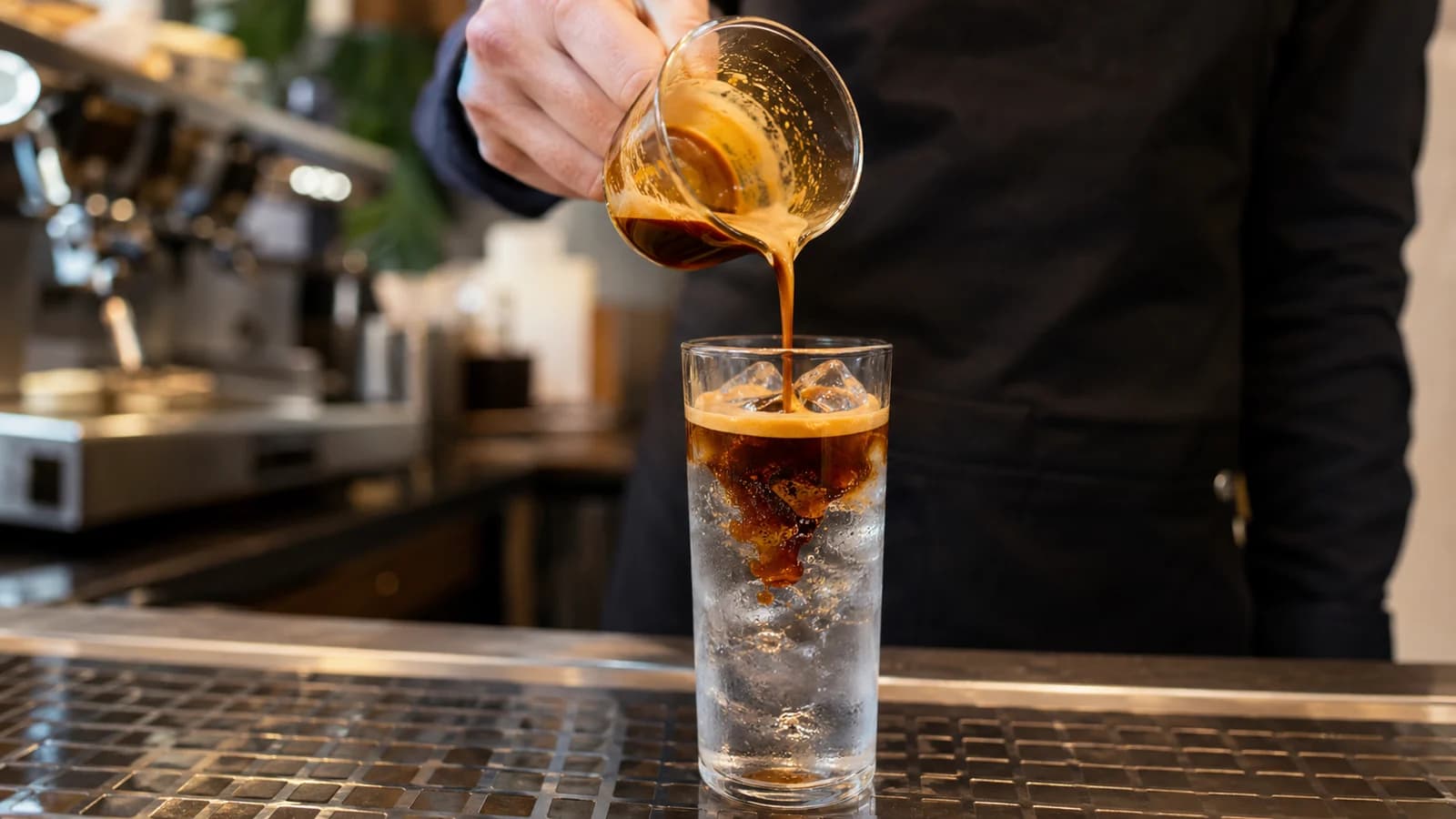 Barista pouring espresso over measured cold water and ice for an iced long black