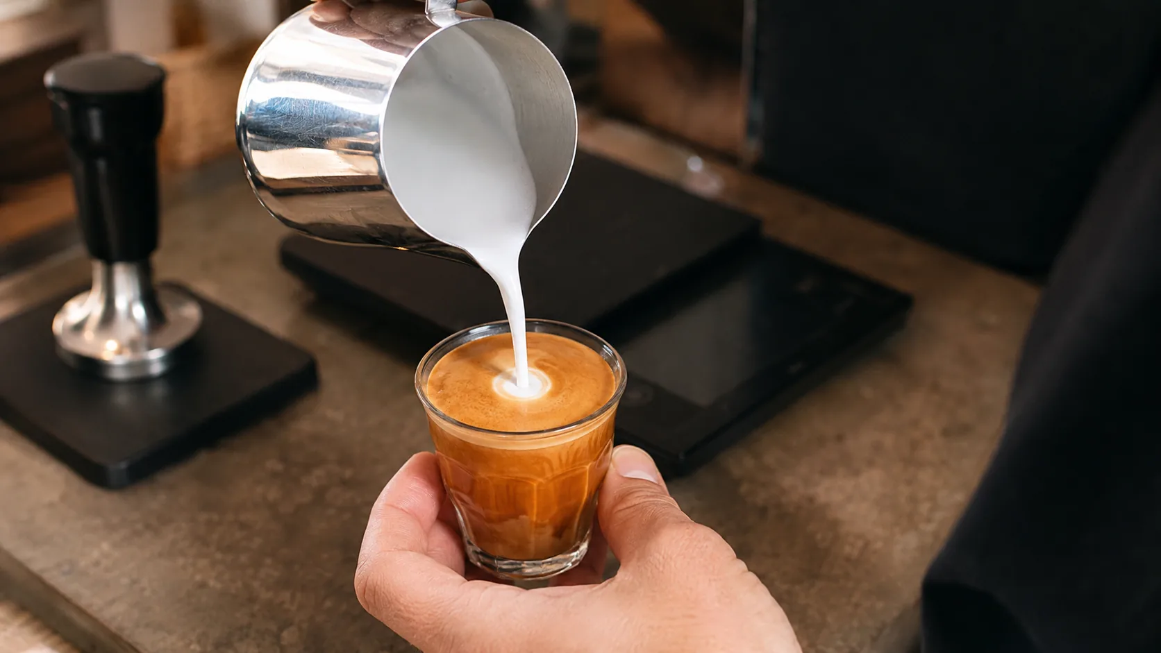 Glossy steamed milk being poured into espresso in a small glass for a piccolo latte