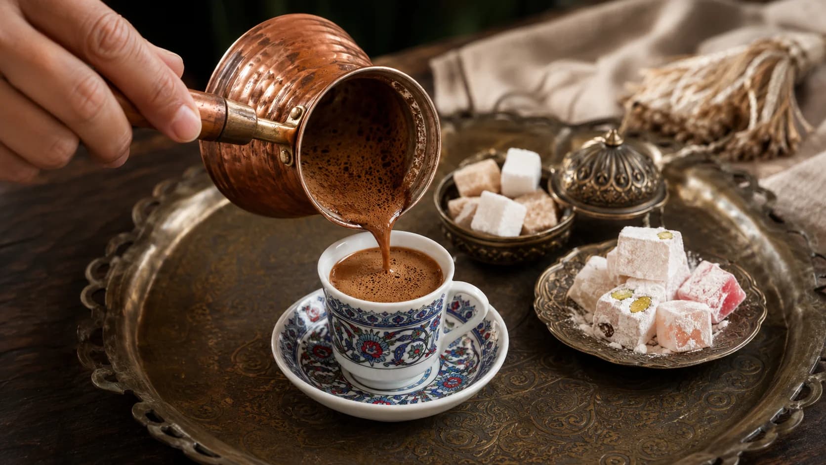 Foamy Turkish coffee being poured from a copper cezve into a patterned demitasse cup