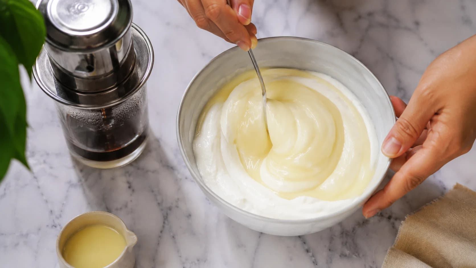 Plain yogurt and condensed milk being mixed while Vietnamese coffee brews through a phin